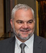 An Australian man with pale grey hair in a white shirt and dark grey jacket and tie is shown.